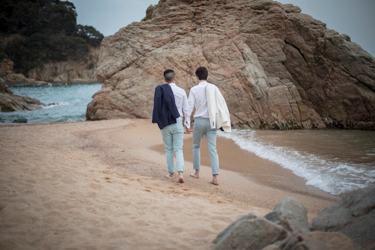 Two gay grooms holding hands and walking on the beach